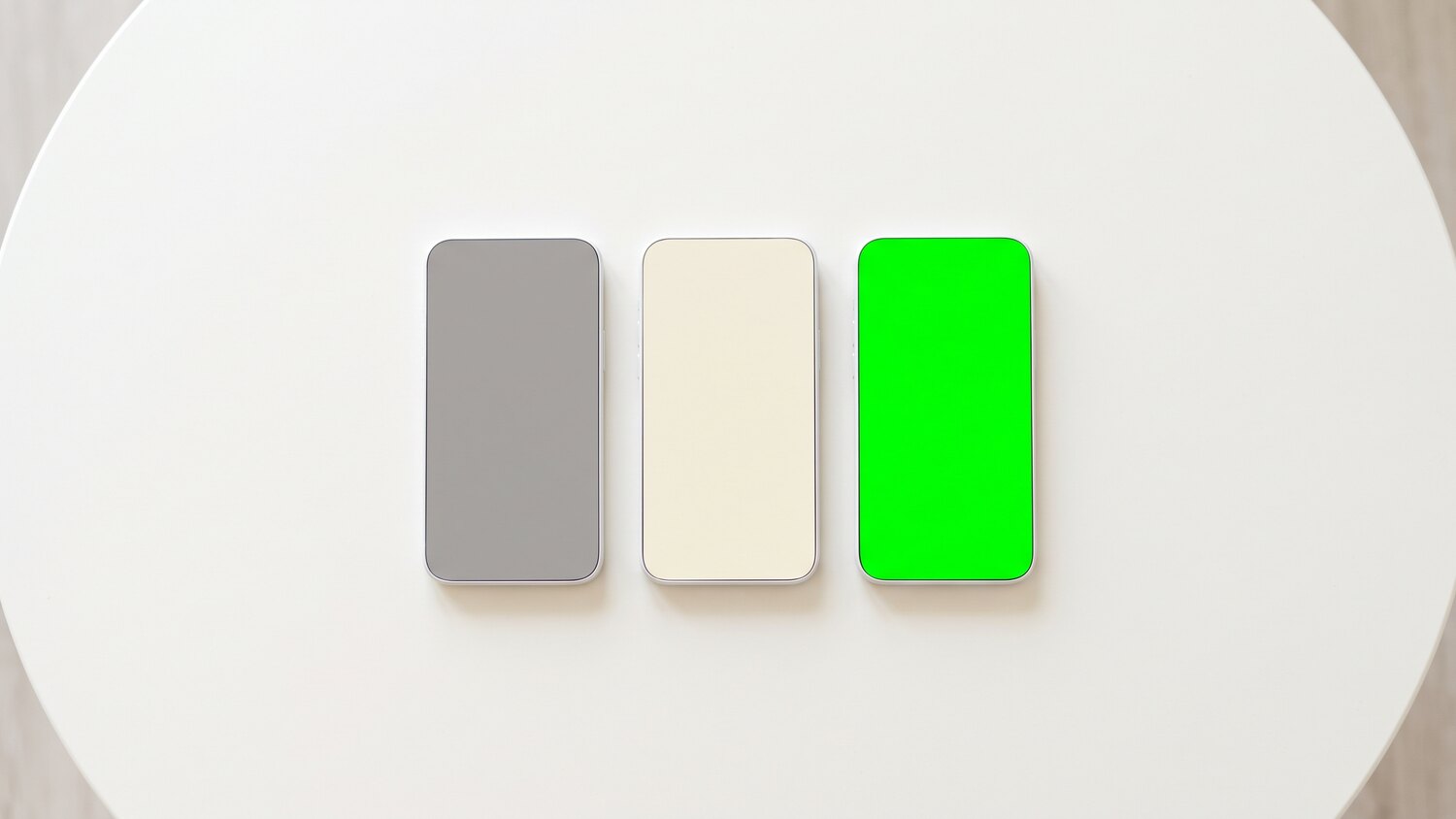 Three identical phones in a row on a white surface with grey, cream and vivid green blank screens